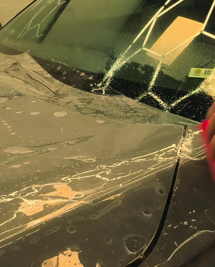 Paint protection film being laid on a dark car under the shop's hexagon lights