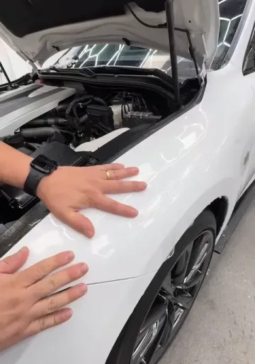 Hands smoothing clear film over a white hood, hexagon lights reflected in the paint