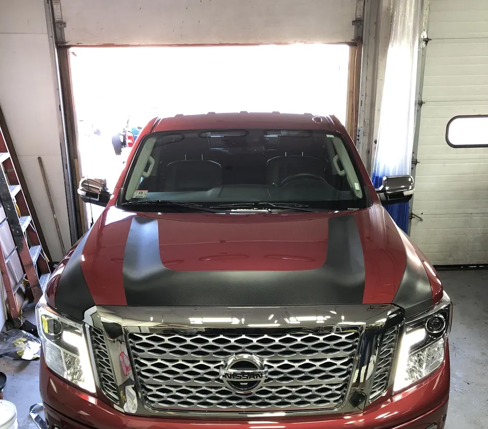 Red Nissan Titan in the bay with a carbon fiber vinyl hood