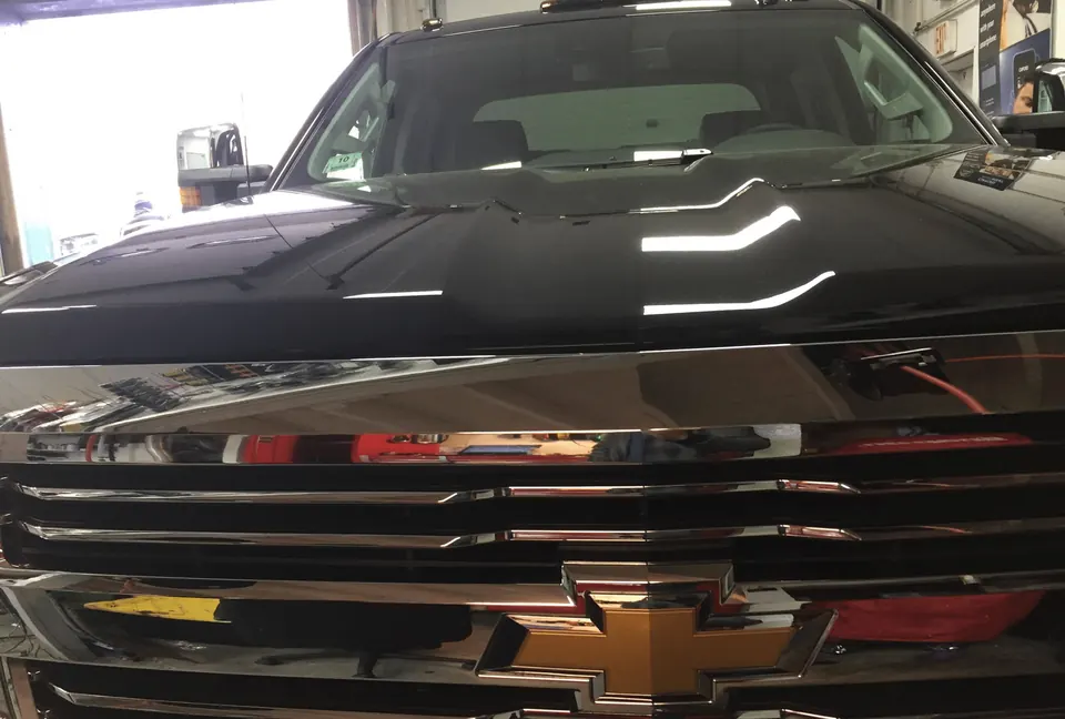 Black Chevrolet pickup with deep, glossy paint, reflecting the shop lights